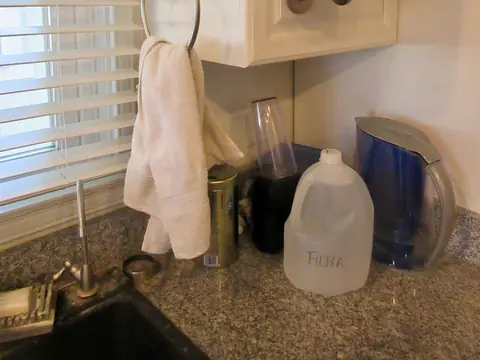 A kitchen sink corner with a filter pitcher and a jug of filtered water