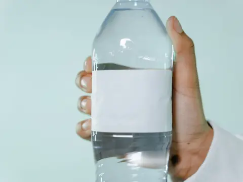 A clear bottle of water with a blank label, held up to the light