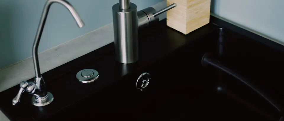 A kitchen sink with a stainless faucet and a small separate drinking water faucet