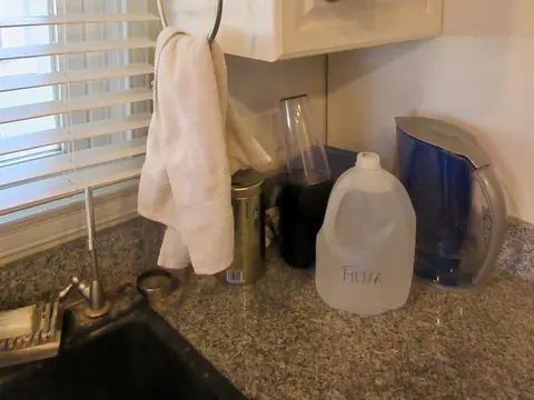 A kitchen sink corner with a filter pitcher and a jug of filtered water