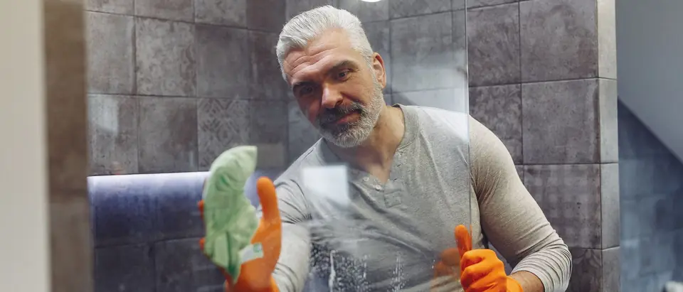 A man in rubber gloves wiping water spots off a glass shower screen