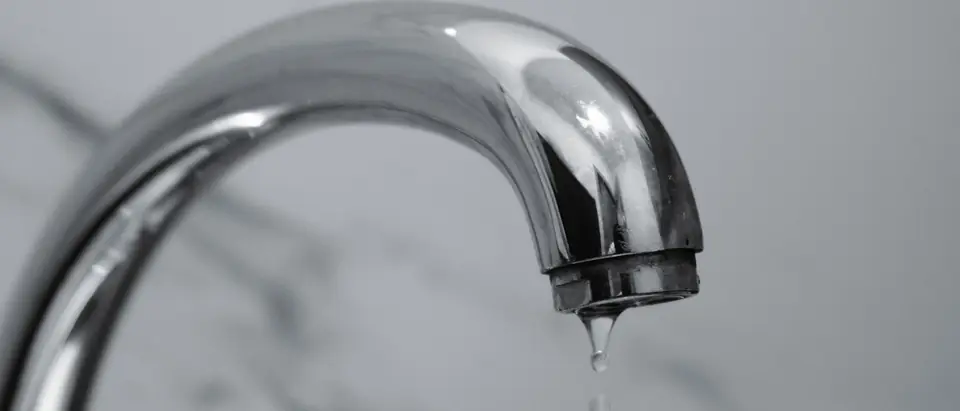 A chrome faucet with a drop of water at its tip