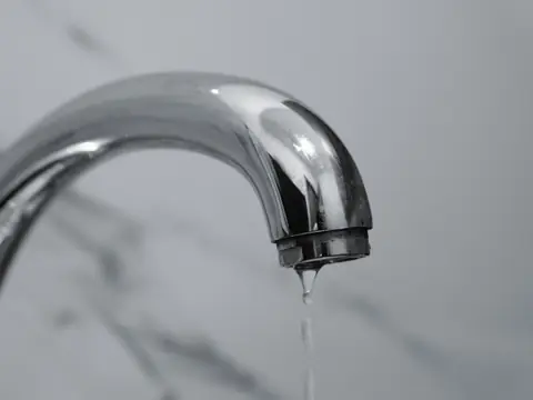 A chrome faucet with a drop of water at its tip